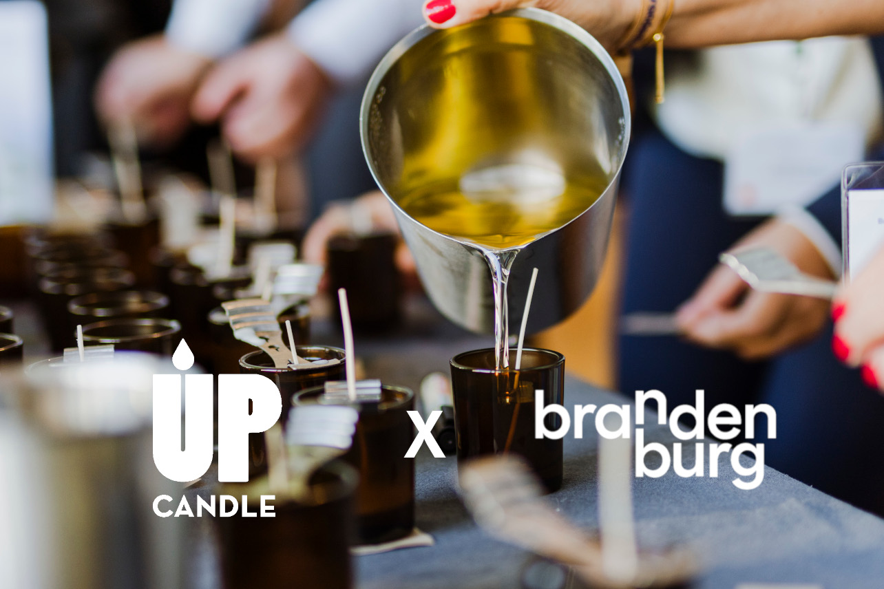 Hand gießt Kerze beim UpCandle Kerzengießworkshop am 29. September 2025 beim Brandenburgischen Tourismustag in Potsdam, daneben die Logos von UpCandle und TMB Brandenburg