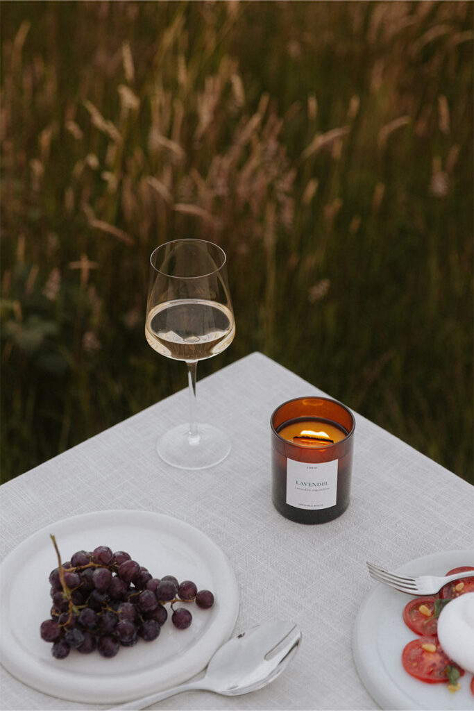 Nahaufnahme einer brennenden UpCandle Aromakerze mit Holzdocht auf einem spätsommerlichen Tisch